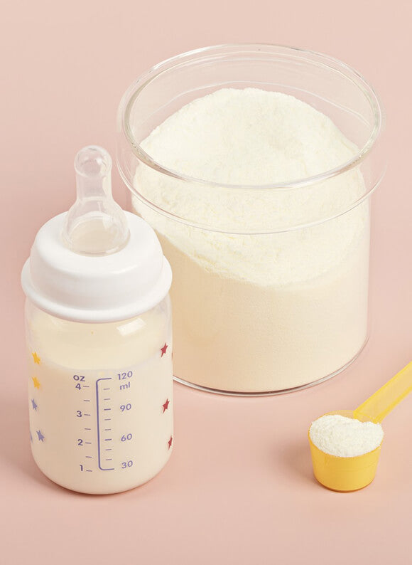 Baby bottle, container of formula, and measuring scoop on a pink background