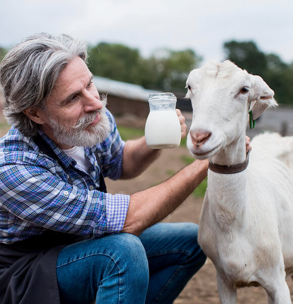 Man holding a glass of milk to a goat outdoors