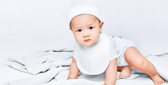 Baby in a white outfit and hat on a white blanket