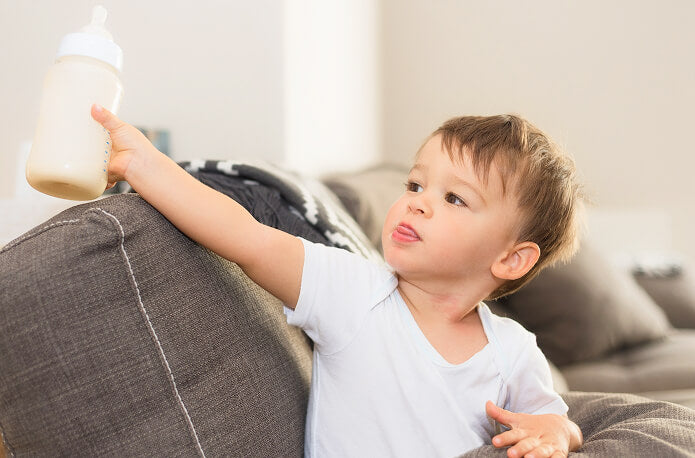 Child holding a bottle on a couch in a home setting