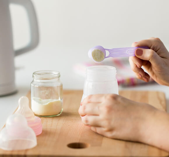 Person measuring powder into a jar with a spoon on a wooden surface