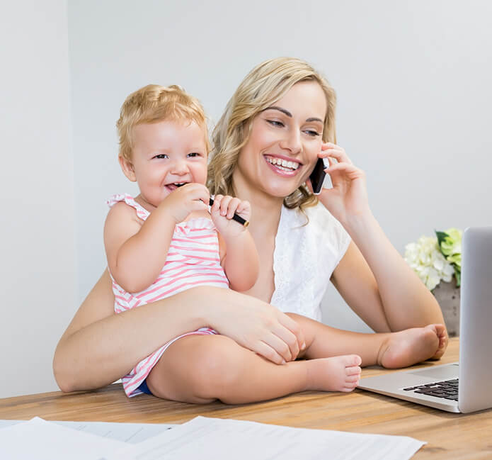 Woman on phone with baby on lap at a desk with laptop