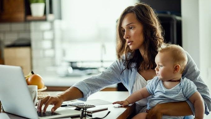 Mother holding her baby at the kitchen table while ordering European organic baby formula online on her laptop
