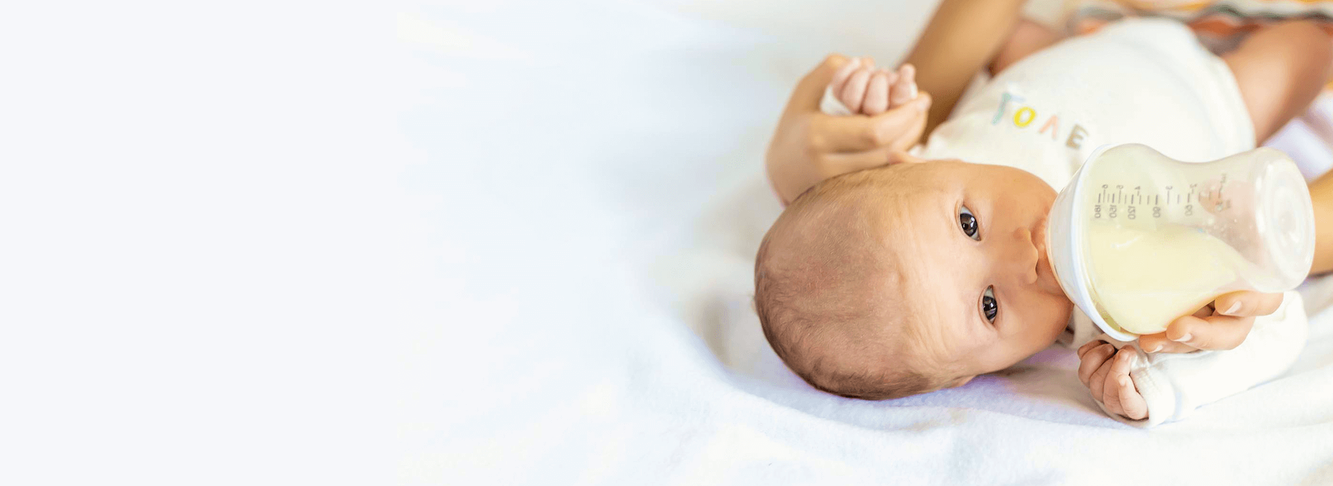 Baby lying on a white surface with a bottle in hand