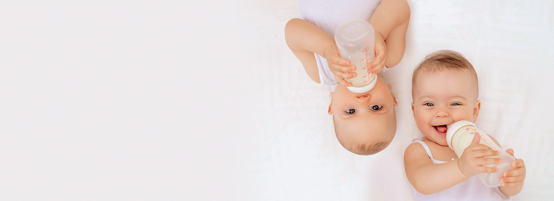 Two babies holding bottles on a white background